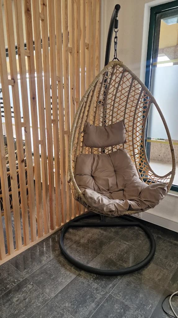Cadeira suspensa de vime com almofadas bege, junto a uma divisória de ripas de madeira